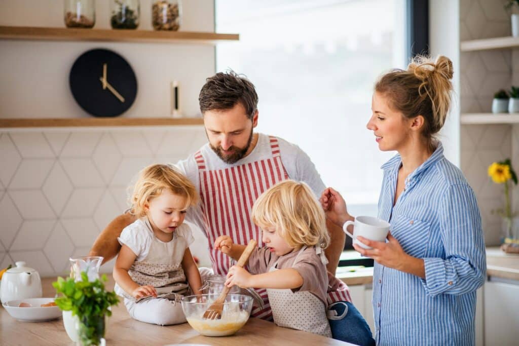 Eine junge Familie mit zwei kleinen Kindern in einer Küche, die gemeinsam kochen.