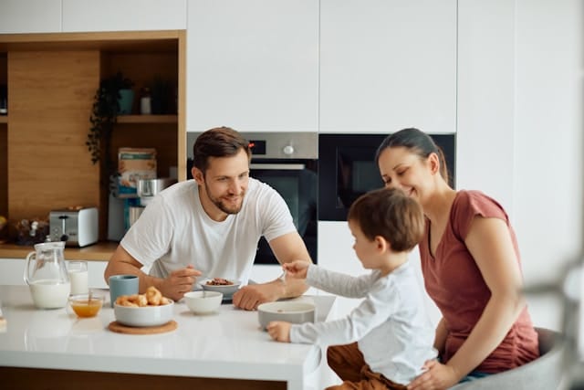 Glückliche Eltern mit ihrem Kleien Sohn frühstücken gemeinsam in der Küche.