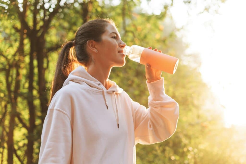 Junge schlanke Frau in Sportbekleidung und einer Trinklasche in der Hand, trinkt ein fitline Fitness-Drink