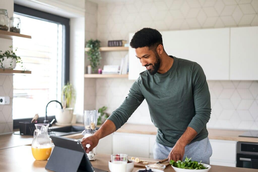 Person kocht in einer modernen Küche und bereitet ein Rezept mit digitaler Unterstützung zu.